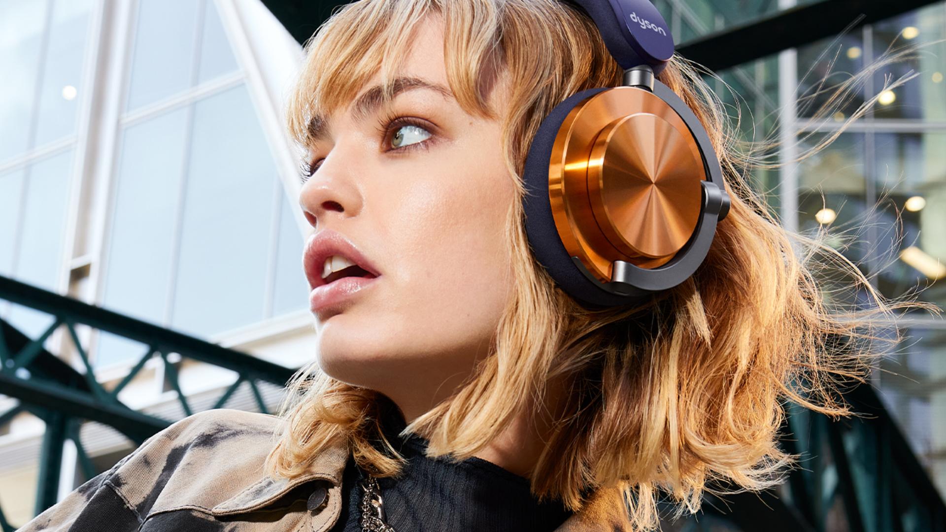 A model wearing Dyson OnTrac headphones with CNC copper outer caps while outside a modern building.