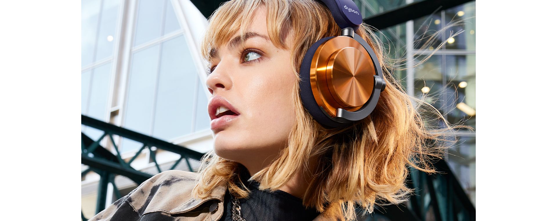 A model wearing Dyson OnTrac headphones with CNC copper outer caps while outside a modern building.
