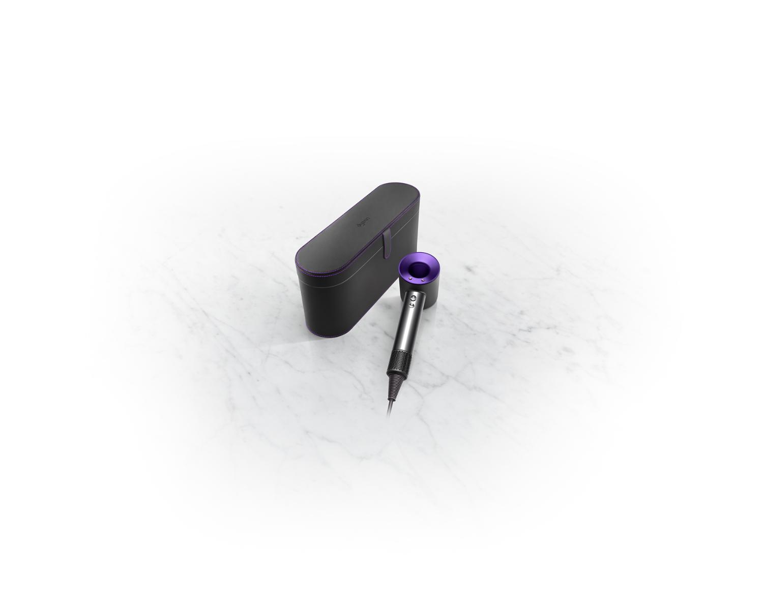 The Dyson Supersonic Black/Purple hair dryer resting next to a Black presentation case
