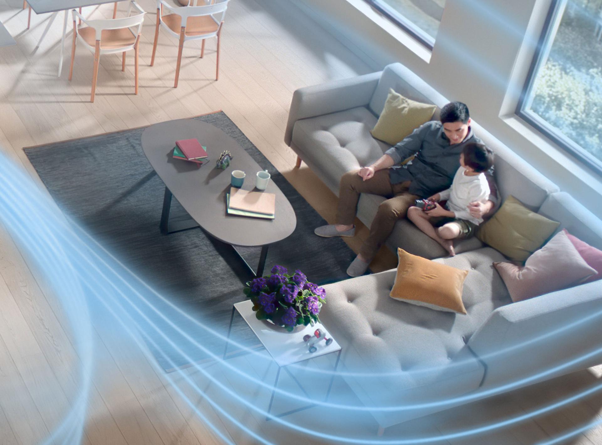 Ojciec z synem siedzący w salonie na kanapie z włączonym oczyszczaczem powietrza Dyson, który rozprowadza oczyszczone powietrze po pomieszczeniu