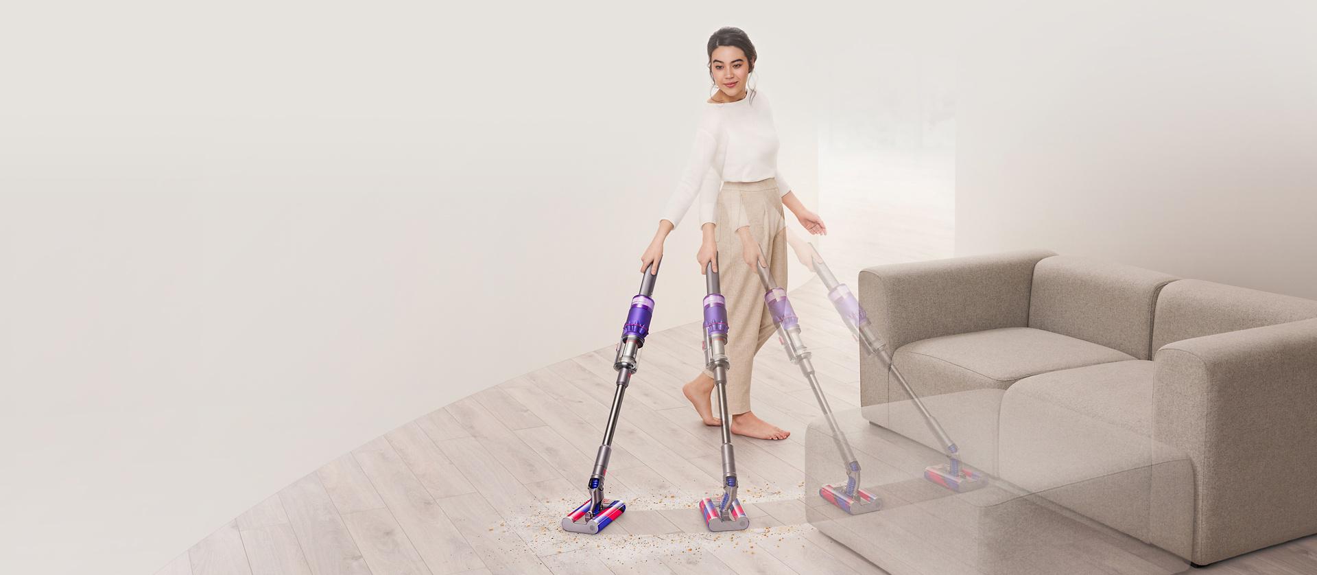 Mujer aspirando piso duro alrededor de un sofá con la aspiradora Dyson Omni-glide™.