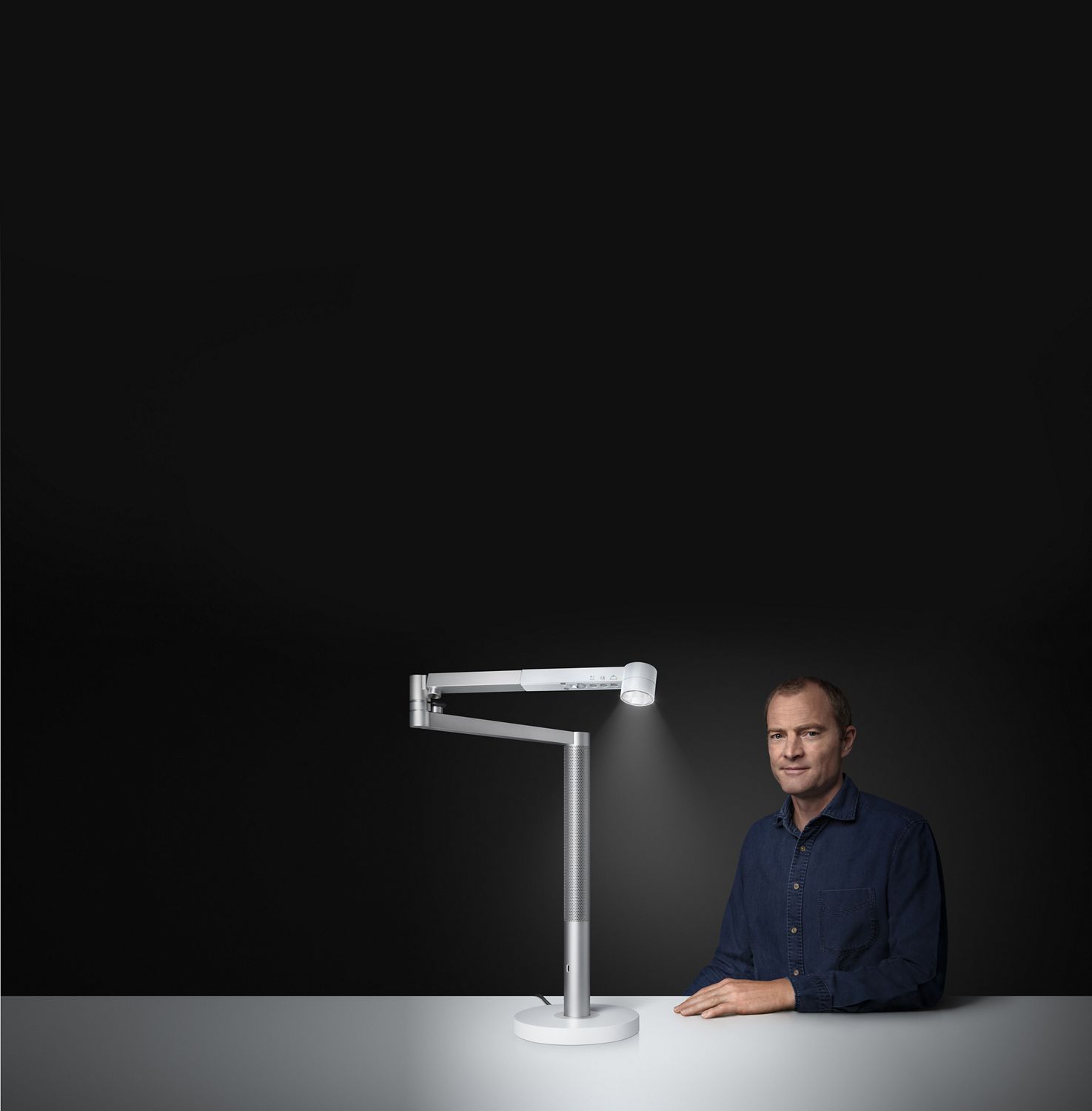 Jake Dyson assis à côté de la lampe de travail Dyson Solarcycle🅪