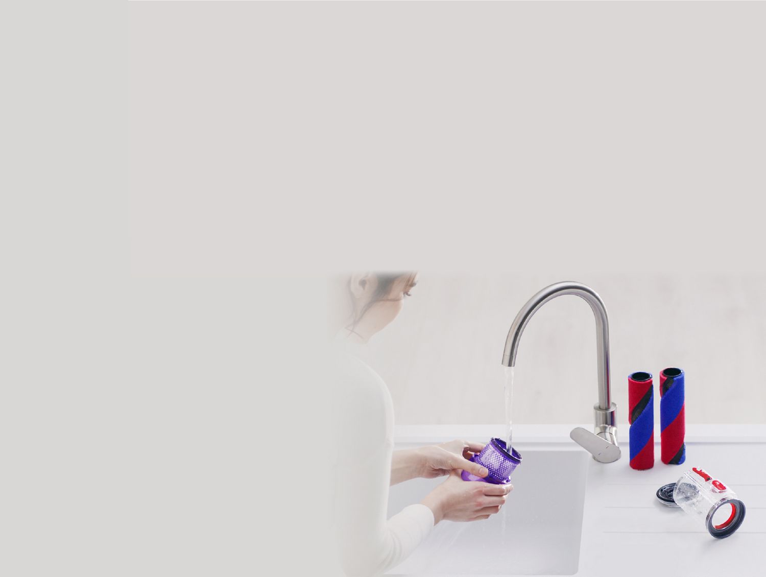 Brush bars, clear bin and worktop tool on a draining board while filter is being washed under running water.