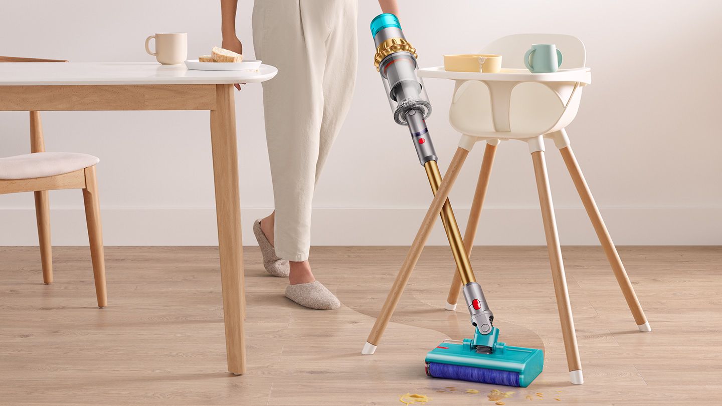 Dyson vacuum picks up debris from hard floor. A baby seat is in background. 