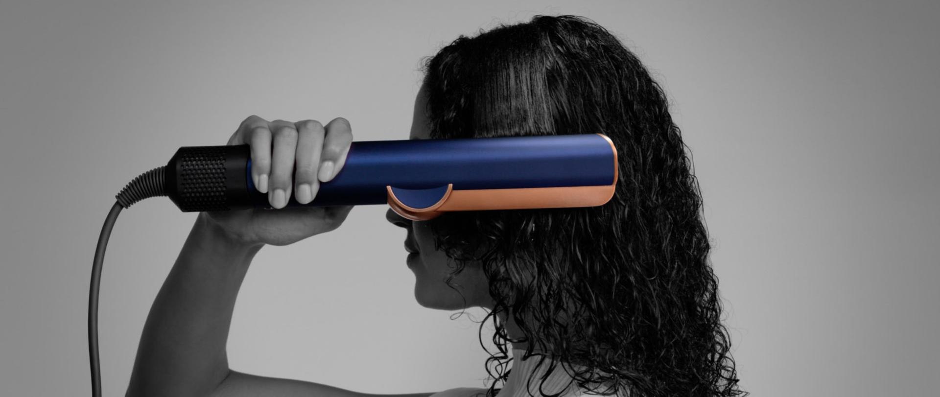 A woman using a Dyson Airstrait straightener to dry and straighten a tress of her hair.